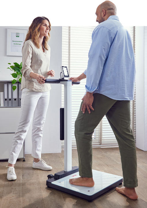Practitioner assisting a client standing on the seca mBCA Alpha analyzer platform during a body composition scan